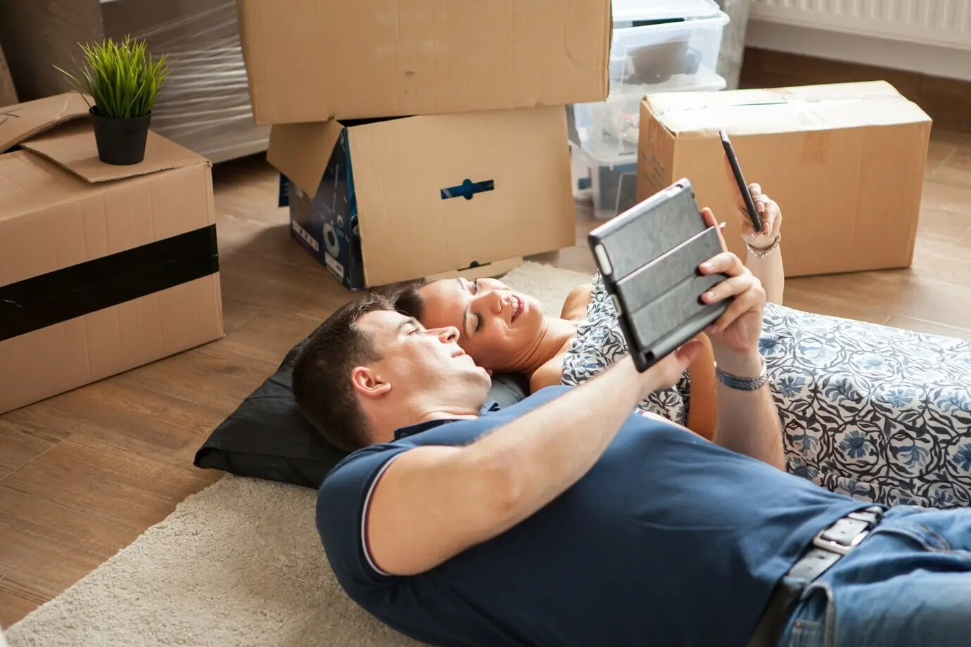 A happy couple lies on the floor after moving in; the man and woman are smiling.