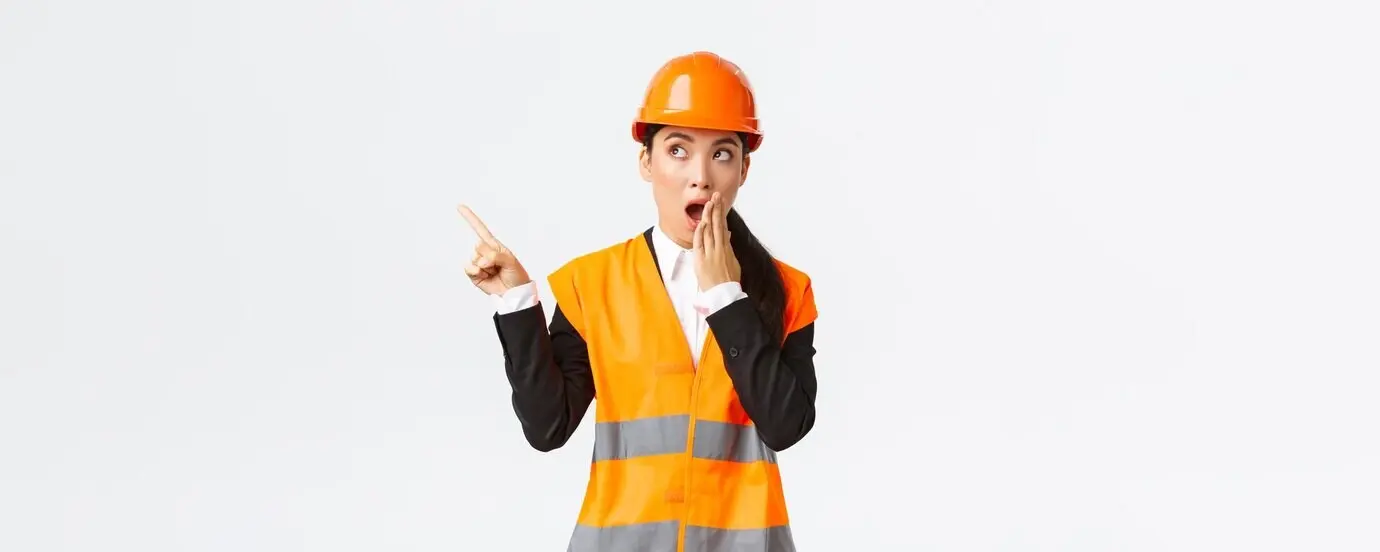 An astonished and impressed Asian female engineer and construction manager wearing a safety helmet and reflective jacket, gasping and pointing a finger toward the upper left corner, amazed after discovering something interesting.